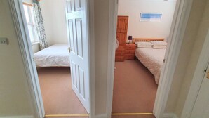Un dormitorio con dos camas individuales, un armario de madera, una mesita de noche con lámpara y un cuadro en la pared.