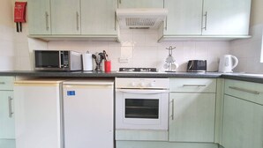 Una cocina con armarios verde claro, un refrigerador blanco, un microondas, una estufa y un hervidor.