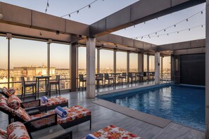 An indoor swimming pool area with lounge chairs and tables, large windows offering a city view, and a modern architectural design. - Courtyard by Marriott Amritsar (Amritsar)
