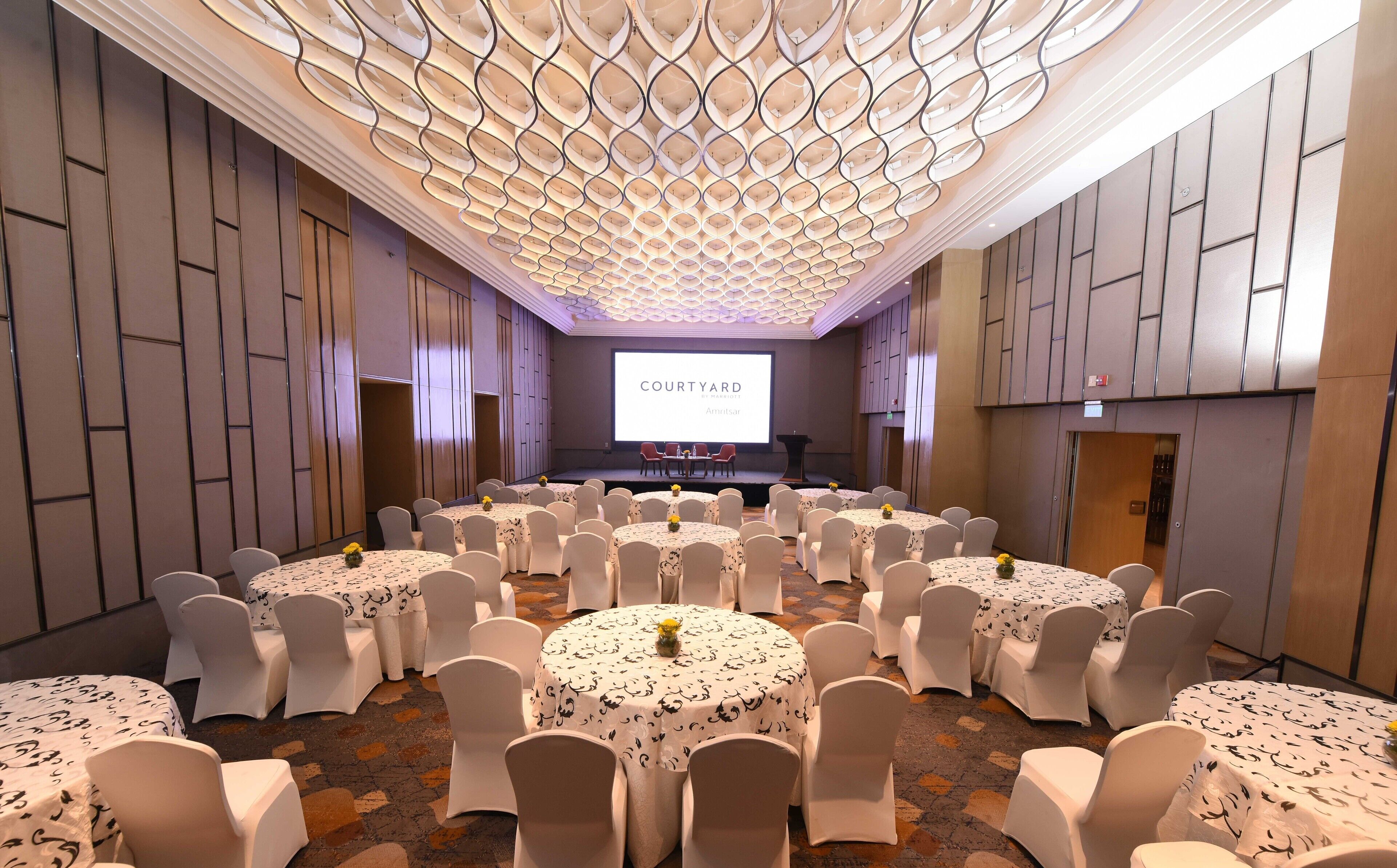 A conference room with a stage, multiple tables with chairs, and a large screen displaying "COURTYARD".