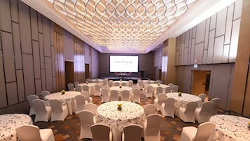 A conference room with a stage, multiple tables with chairs, and a large screen displaying "COURTYARD".