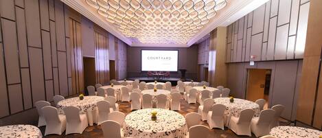 Un salón de conferencias con un escenario, varias mesas con sillas y una pantalla grande mostrando
