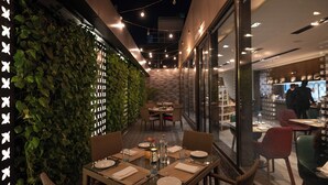 An outdoor dining area with tables set for two, surrounded by a lush green wall and string lights. - Courtyard by Marriott Amritsar (Amritsar)