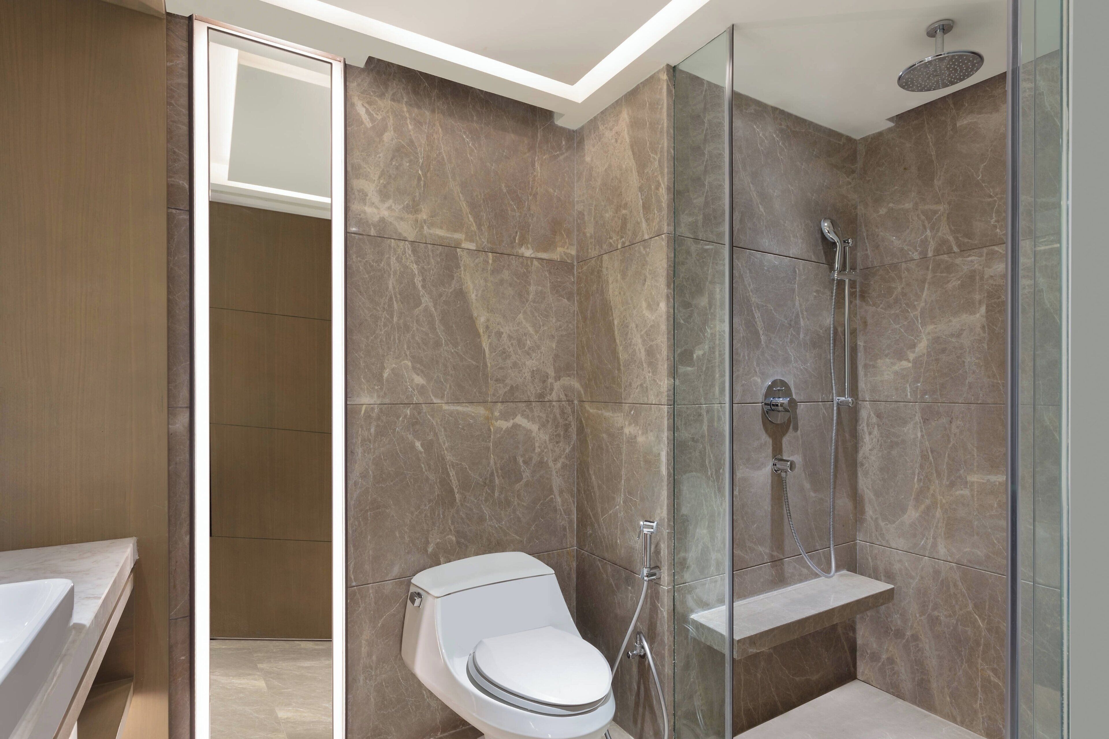 A modern bathroom with a glass-enclosed shower, a toilet, and a marble-tiled wall.