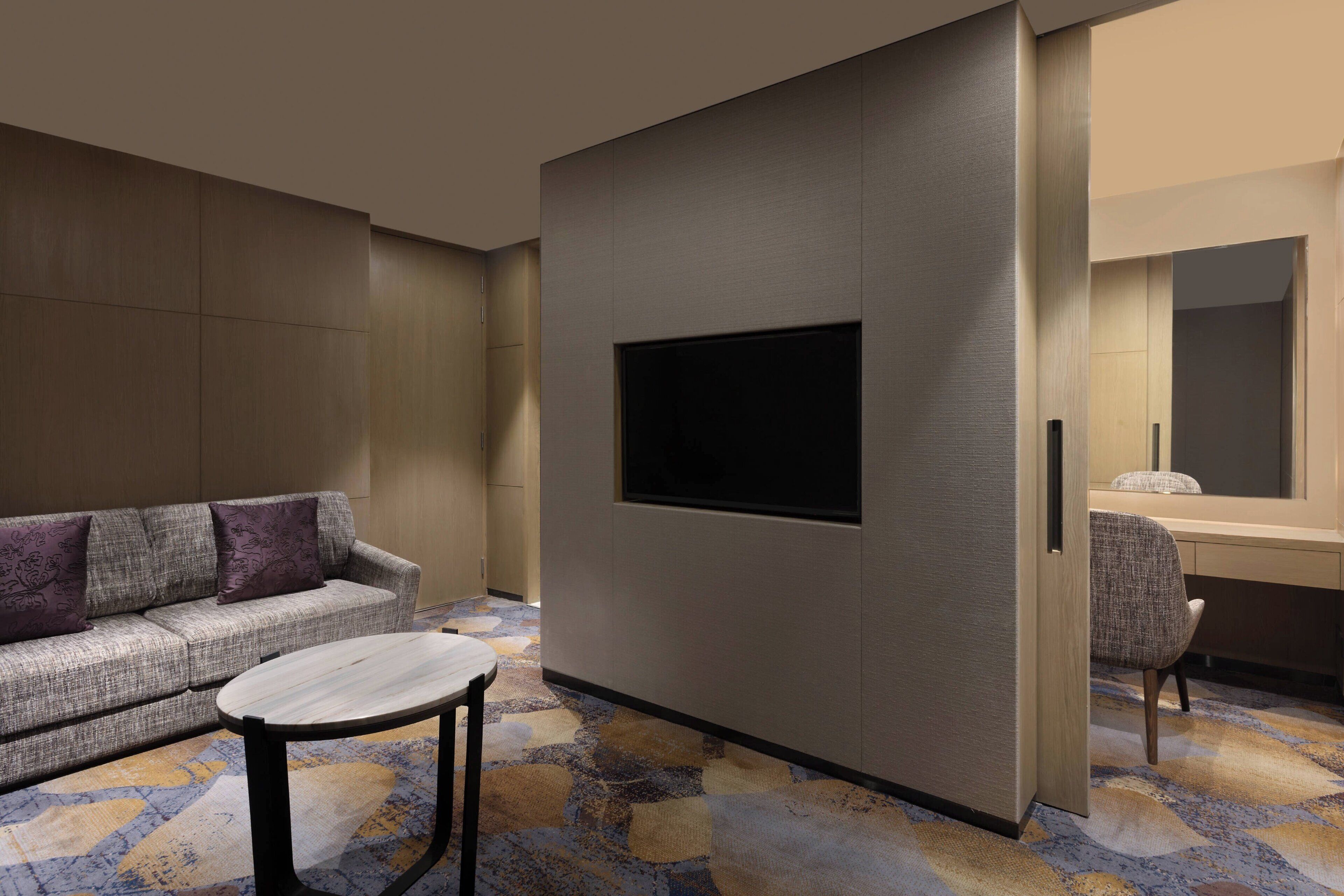 Une chambre d’hôtel moderne équipée d’un canapé, d’une petite table ronde, d’un téléviseur à écran plat fixé au mur et d’un bureau avec une chaise.