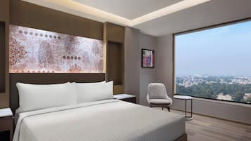 Habitación de hotel moderna con una cama grande, una silla, una mesita y un ventanal con vistas a la ciudad.