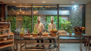 A modern kitchen with chefs, a wooden cart with kitchen tools, and a large window with a green plant wall. - Courtyard by Marriott Amritsar (Amritsar)