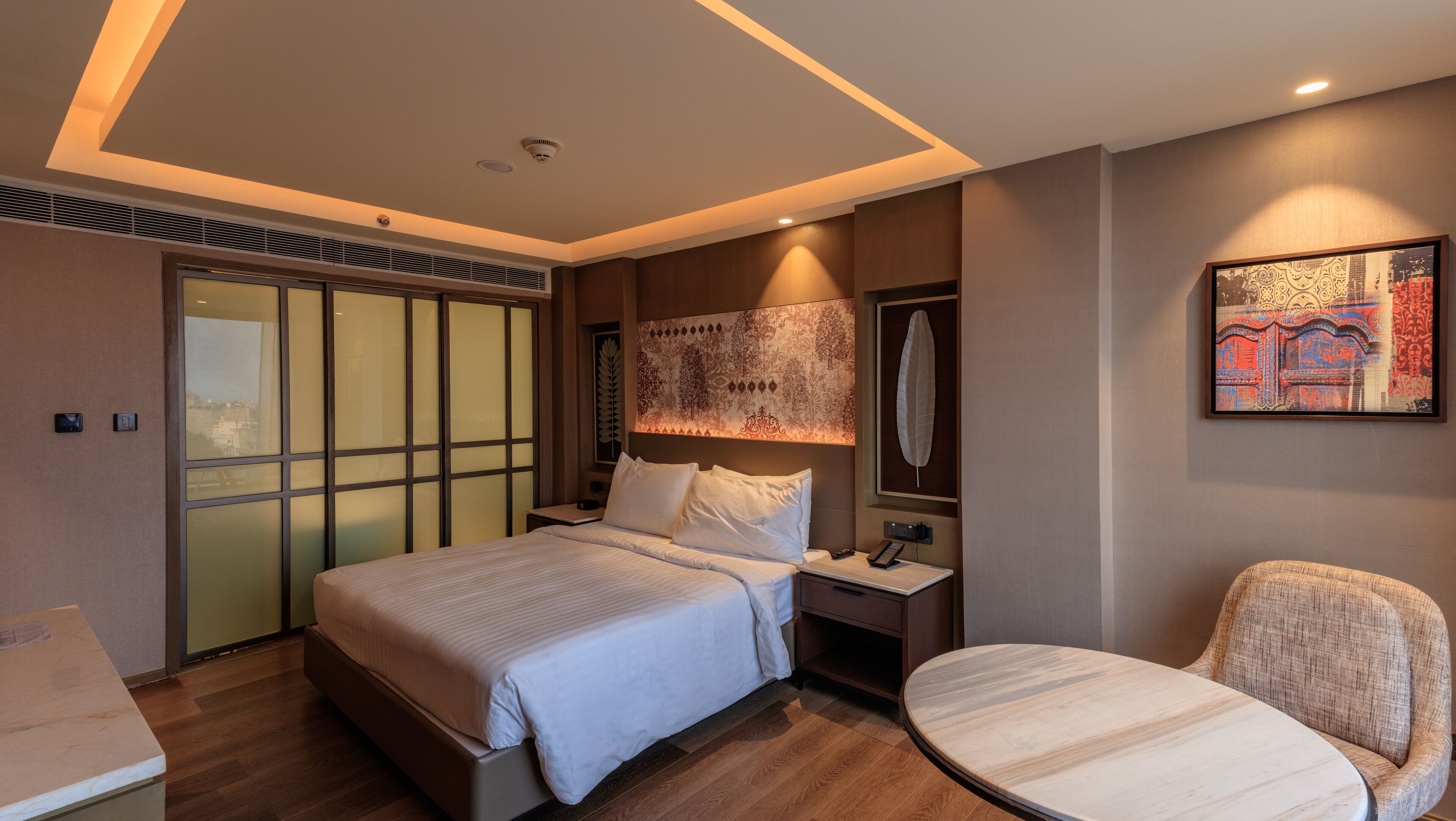 Una habitación de hotel moderna con una cama grande, mesita de noche, silla y un adorno en la pared.