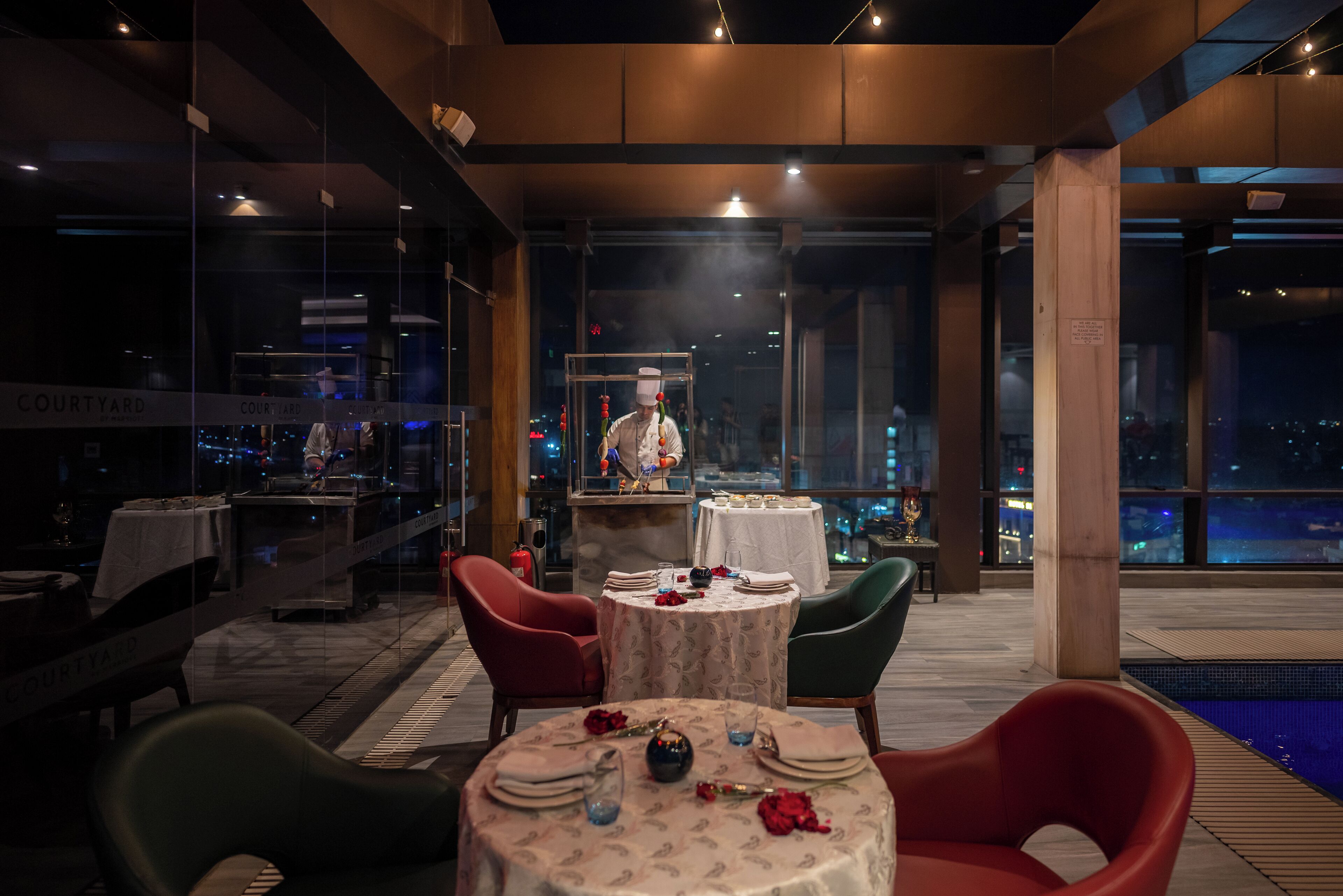 A restaurant with round tables, red and green chairs, and a view of the city at night.