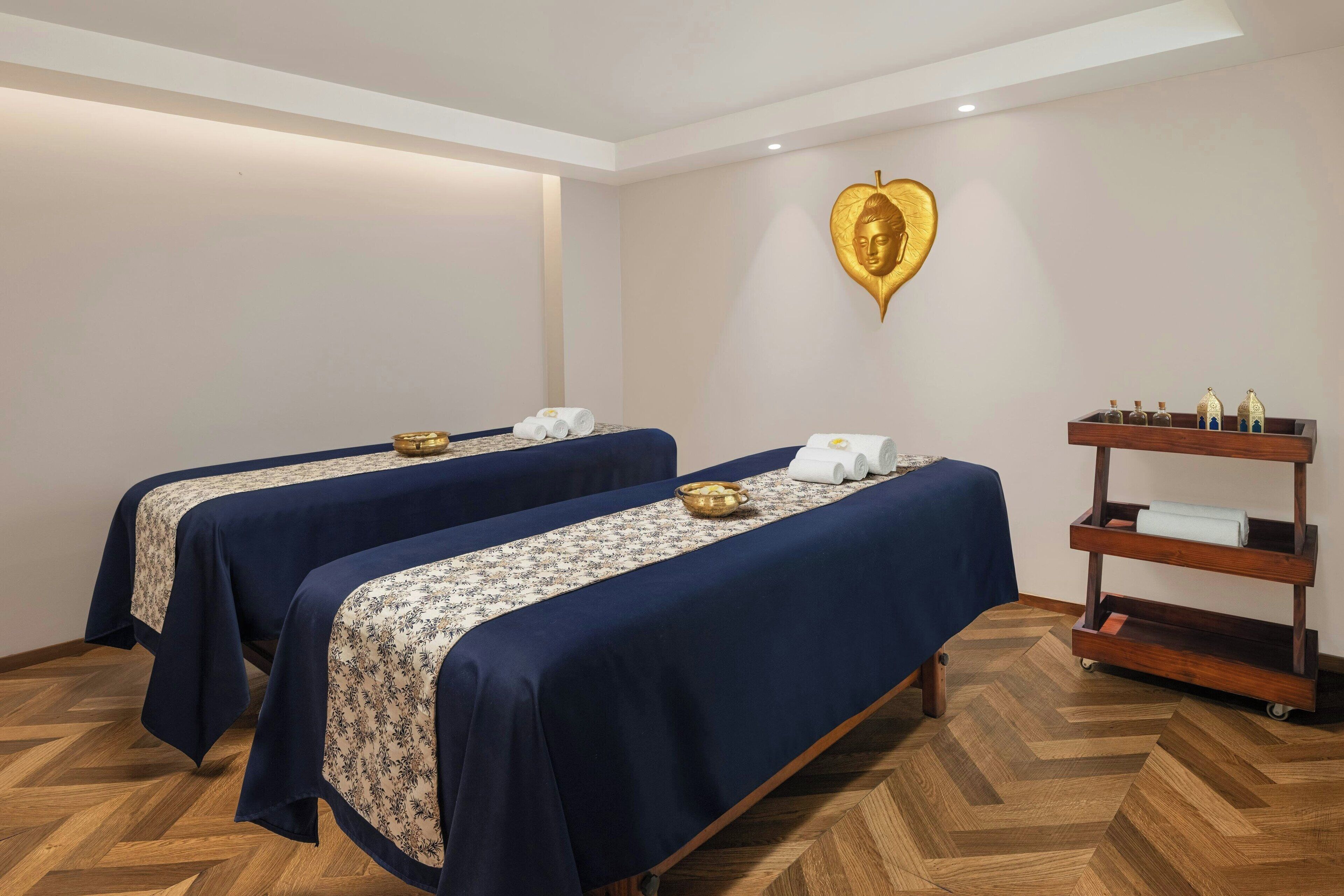 A room with two beds, a wooden floor, a wall-mounted shelf with bottles, and a heart-shaped decoration.
