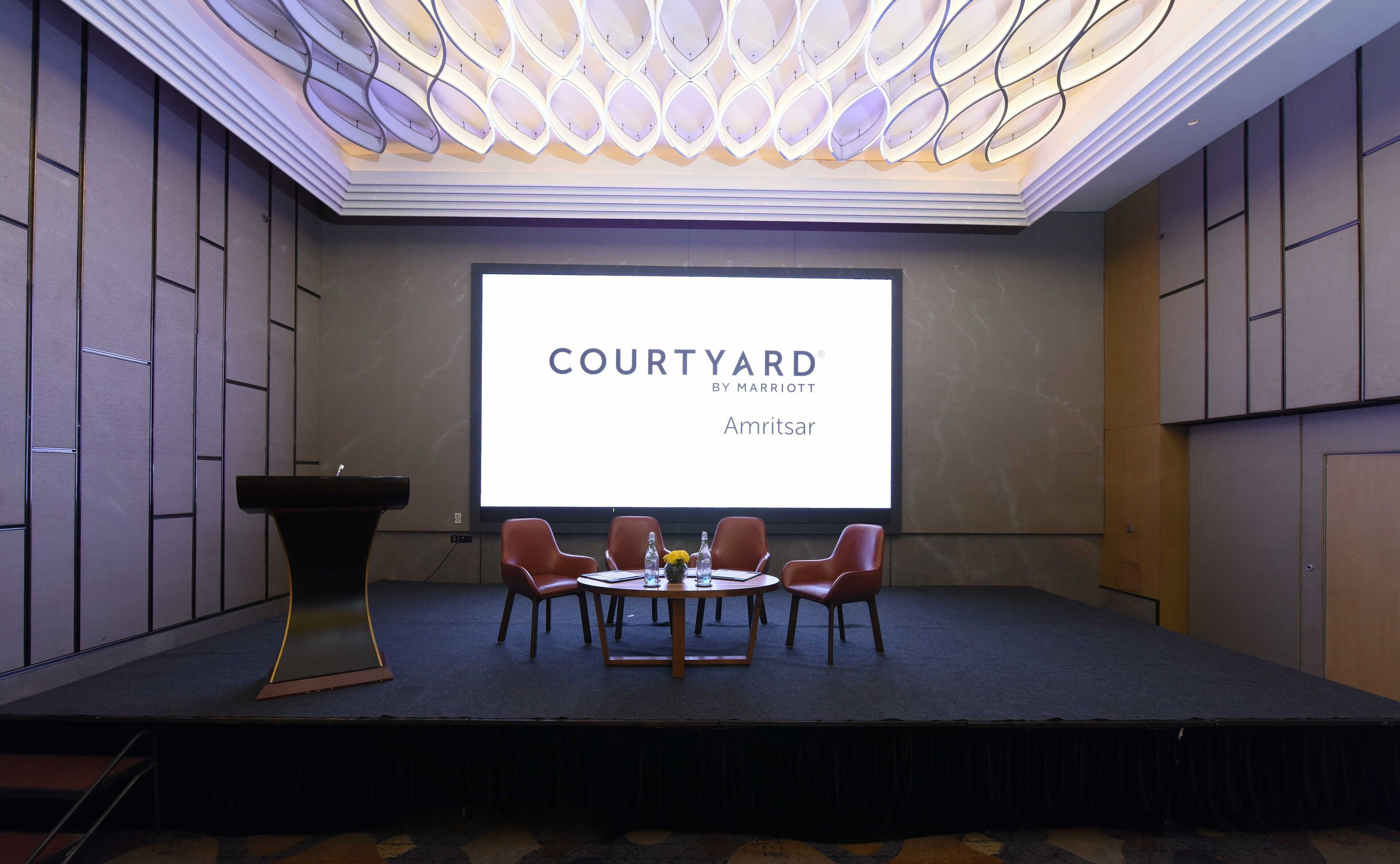 A conference room with a large screen displaying "COURTYARD BY MARRIOTT Amritsar".