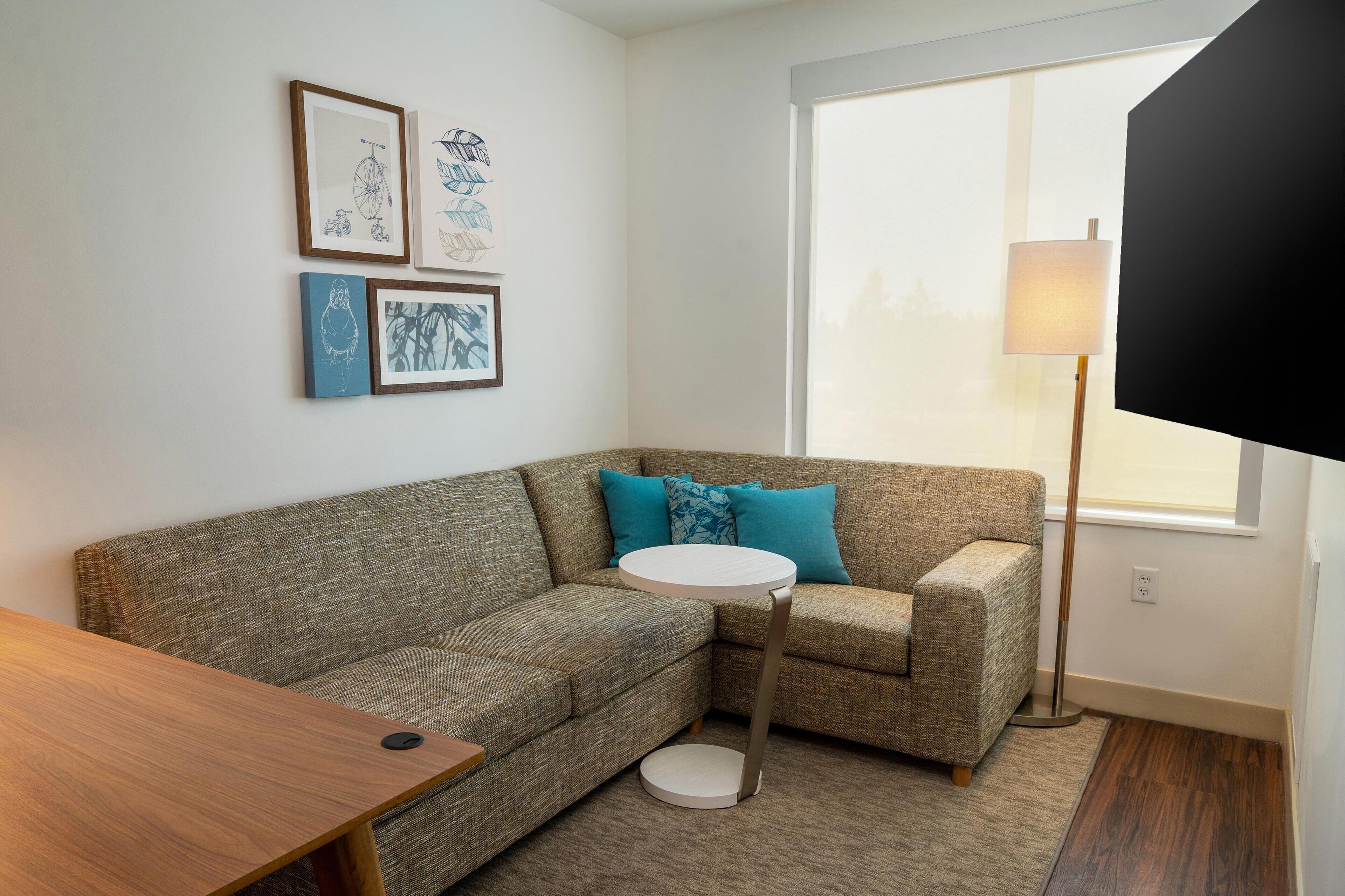 A corner living room with a sectional sofa, a small round table, and framed artwork on the wall.