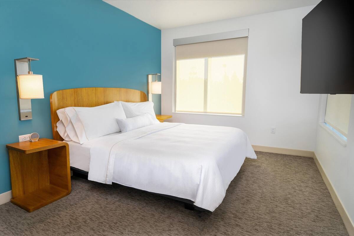 Una habitación de hotel con una cama, dos lámparas de noche, un televisor y una ventana con persianas.