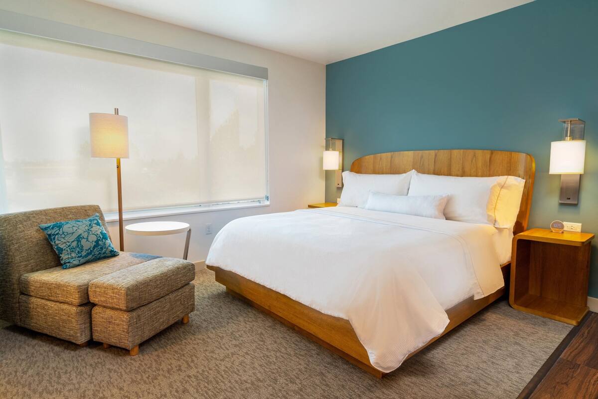 Una habitación de hotel con una cama grande, un sofá con un cojín, una lámpara y una mesita de noche.