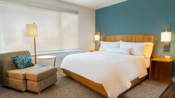 A hotel room with a large bed, a sofa with a pillow, a lamp, and a nightstand.