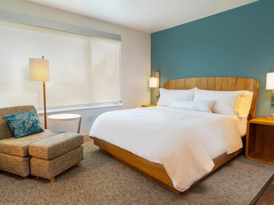 A hotel room with a large bed, a sofa with a pillow, a lamp, and a nightstand.