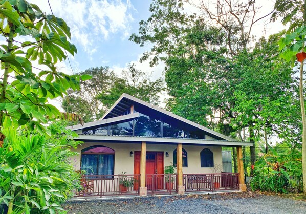 Uma casa de dois andares com porta vermelha, varanda e varanda coberta.