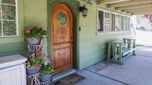 A green house with a wooden front door, potted plants, and a bench outside.