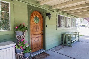 A green house with a wooden front door, potted plants, and a bench outside.