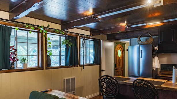 A cozy room with a wooden ceiling, a dining area with a long table, and a kitchen with a refrigerator and cabinets.