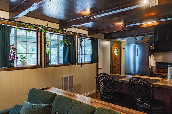 A cozy room with a wooden ceiling, a dining area with a long table, and a kitchen with a refrigerator and cabinets.
