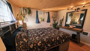 A bedroom with a bed, a desk, a mirror, and various plants.