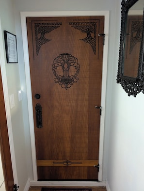 A wooden door with a carved tree design, a mirror, and a framed sign on the wall.