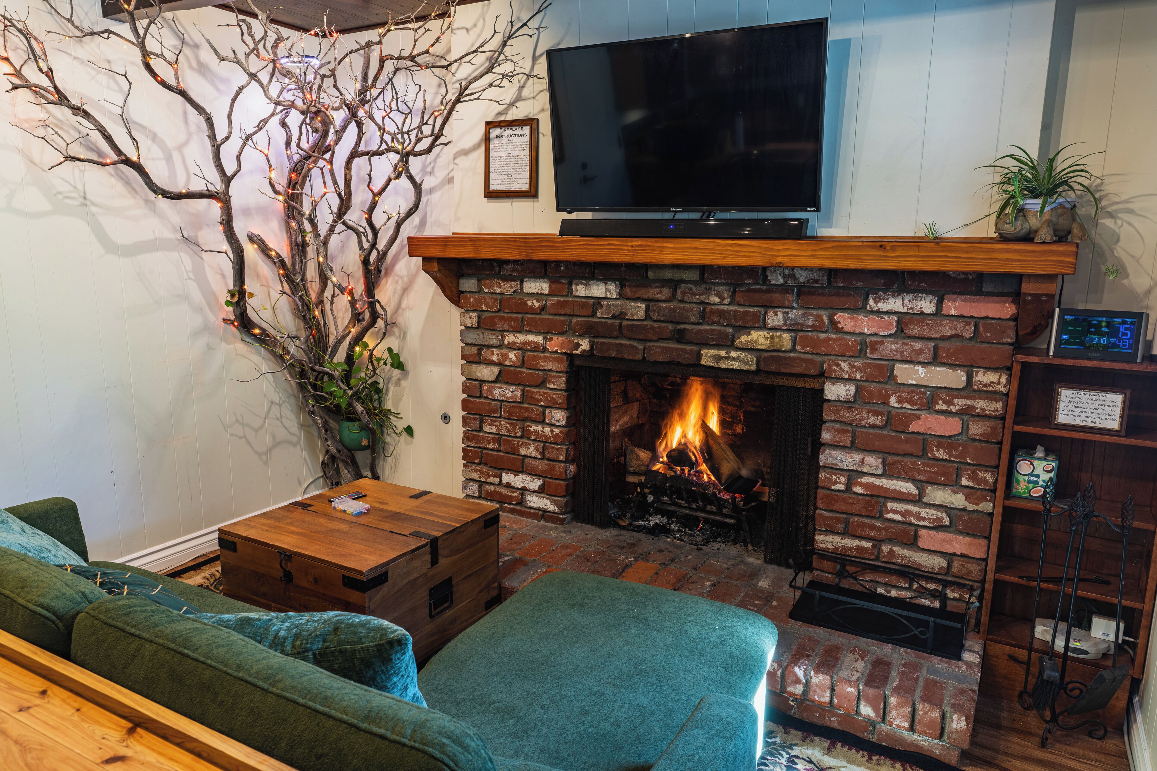 A living room with a brick fireplace, a flat-screen TV mounted above it, a green sofa, and a wooden coffee table.