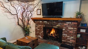 Un salon avec une cheminée en briques, un téléviseur à écran plat fixé au-dessus, un canapé vert et une table basse en bois.