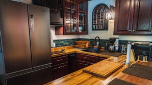 A kitchen with dark wooden cabinets, a stainless steel refrigerator, a wooden countertop, and a coffee maker.
