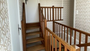 Un escalier en bois avec une rampe, menant à un palier doté d’une porte blanche et d’un papier peint à motifs.