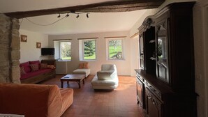 Un salon avec un mur en pierre, un plafond en bois, un téléviseur, un canapé, un fauteuil et un meuble.
