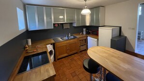 Une cuisine compacte équipée d’un évier, d’une cuisinière et d’un four à micro-ondes. Elle comprend un plan de travail en bois et un tabouret de bar.