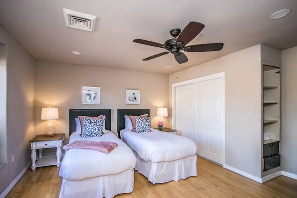 A bedroom with two beds, a ceiling fan, a white wardrobe, and a small bedside table with a lamp.
