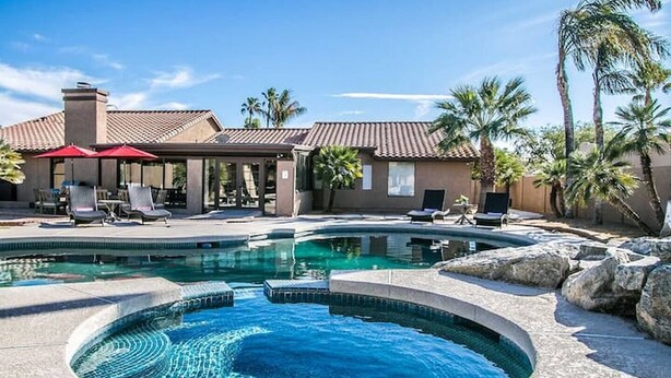 Une piscine avec un jacuzzi, des chaises longues et des palmiers.
