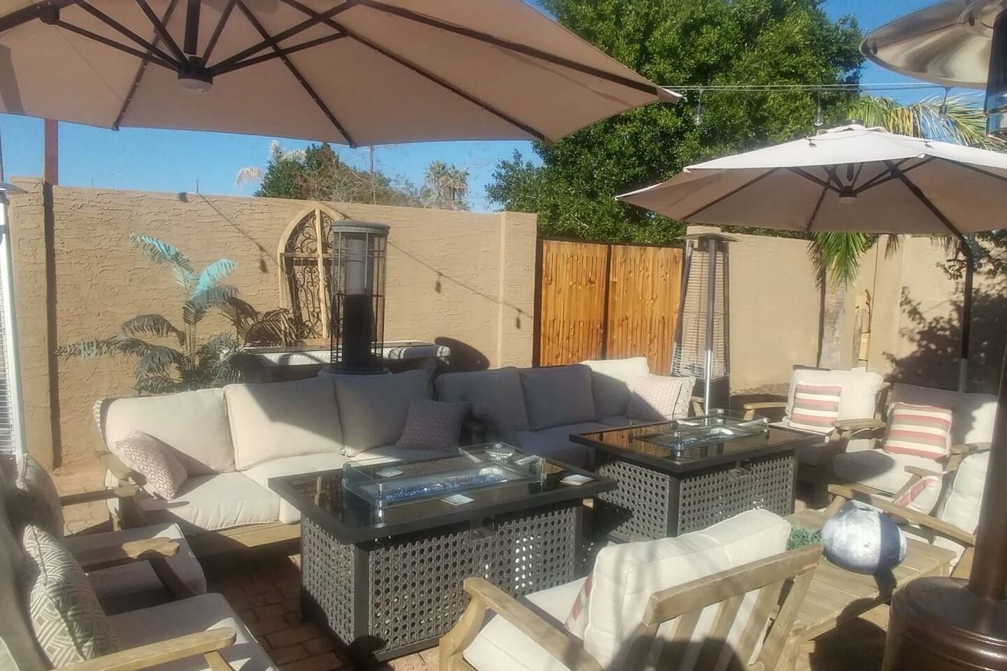 An outdoor patio area with a sofa, two side tables, and a chair under a large umbrella.