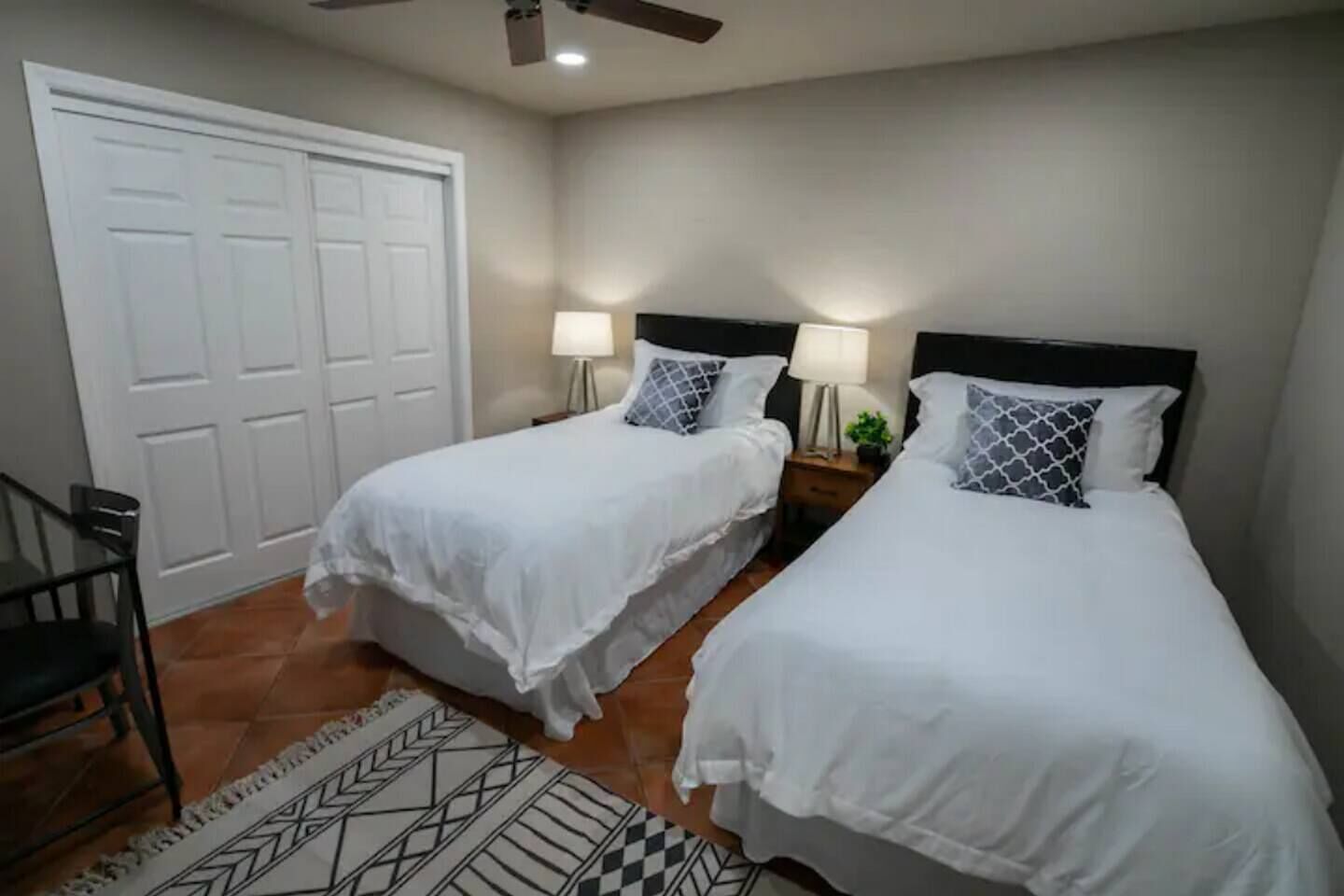 A hotel room with two single beds, a desk, a chair, and a door.
