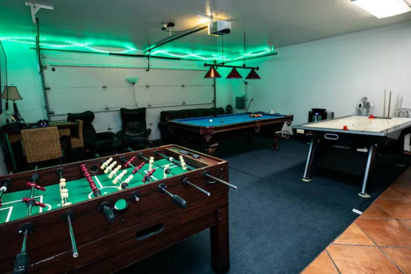 A room with a foosball table, pool table, and a billiards table.