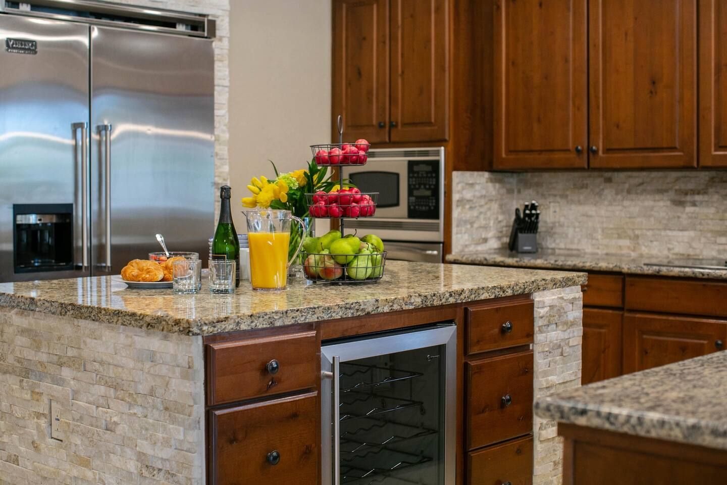 A kitchen with granite countertops, wooden cabinets, a stainless steel refrigerator, a microwave, and a built-in oven.