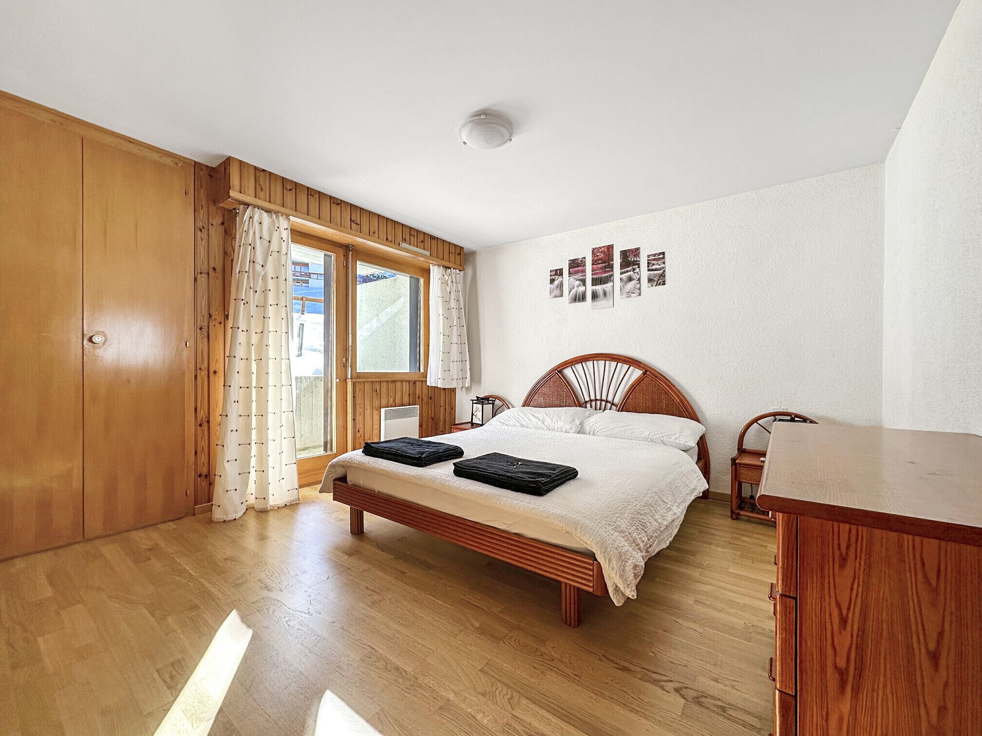 Une chambre à coucher avec un lit en bois, une armoire en bois, un bureau et une fenêtre avec des rideaux.