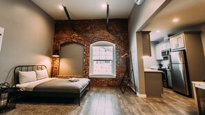 Una camera da letto con parete in mattoni, un letto, un comodino, una lampada e una finestra.