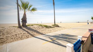 Ein Strand mit Palmen, einem Betonweg und einem 'For Sale'-Schild.