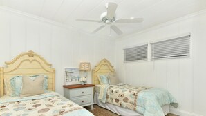 Ein Schlafzimmer mit zwei Betten, einem Deckenventilator und einem Fenster mit Jalousien.