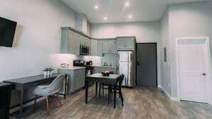 A modern kitchen with grey cabinets, a stainless steel refrigerator, and a dining area with a table and chairs. - Loft apartment in Hollywood (Los Angeles)