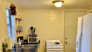 A compact kitchen with a stove, refrigerator, and a small dining area with a chair and table.