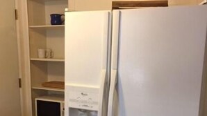 A kitchen with a white refrigerator, a microwave, and a shelf with cups and a blue container.