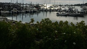 A marina with boats docked under a cloudy sky with the sun visible. - Oceanfront Beach House/ Fall asleep listening to the waves (Scituate)