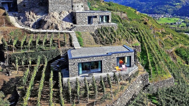 A stone building with a red upper section, a stone lower section, and a small balcony with a chair. - Cà Rossa Suite and Breakfast (Montagna in Valtellina)