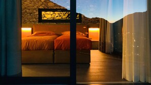 A bedroom with a stone wall, two bedside tables with lamps, a bed with orange bedding, and a view of the sky through a window. - Cà Rossa Suite and Breakfast (Montagna in Valtellina)