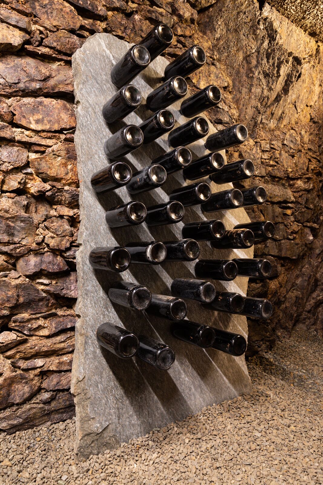 A wine rack made of dark wood with multiple bottles, set against a stone wall.